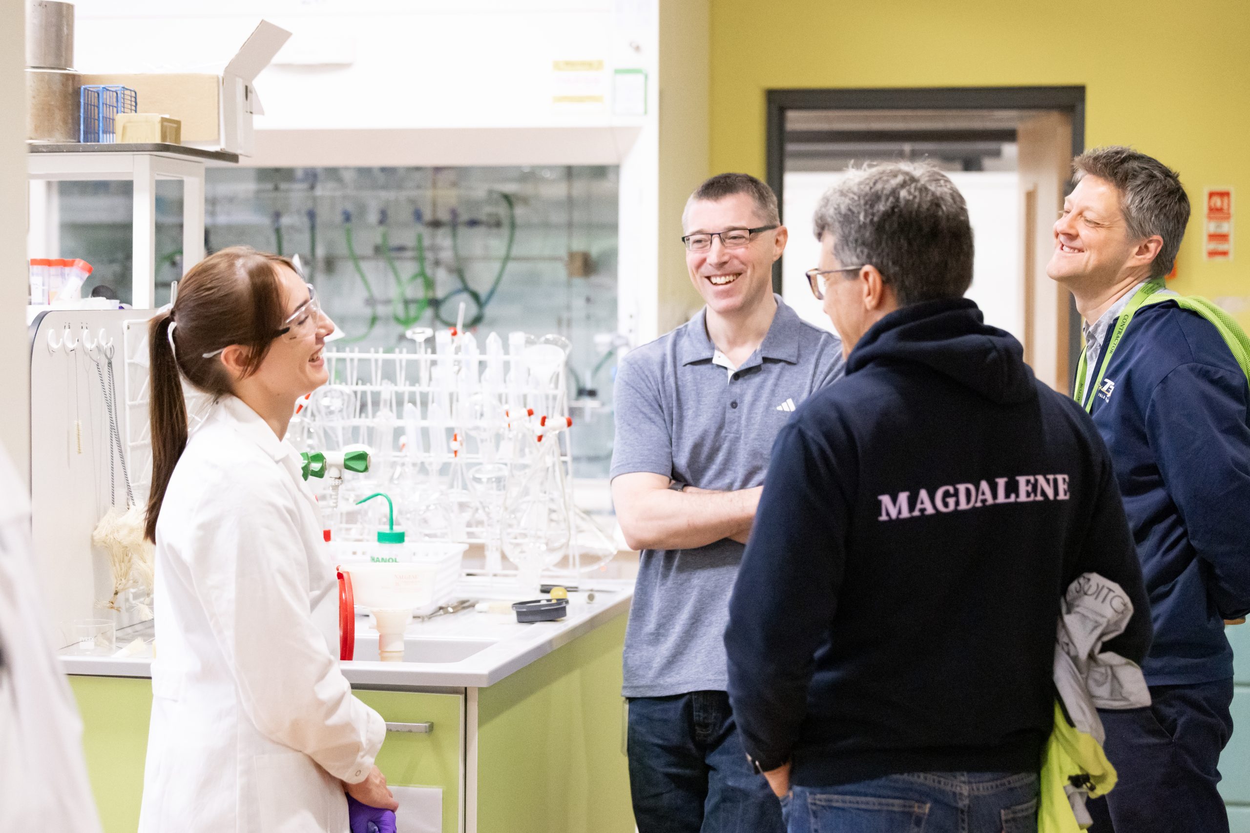4 people in a lab, one in a white lab coat, all deep in discussion