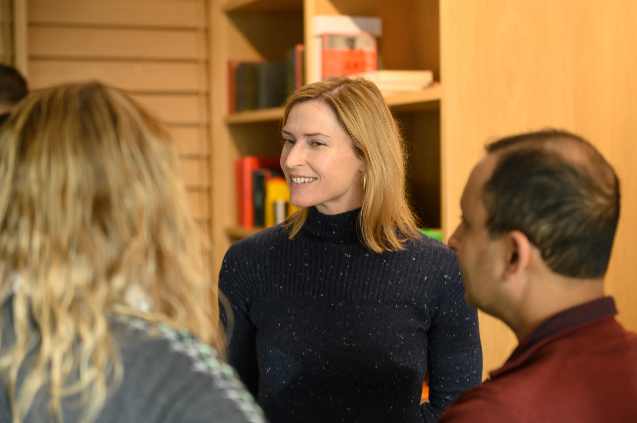 Team smiling and talking in an open room with bookshelves behind