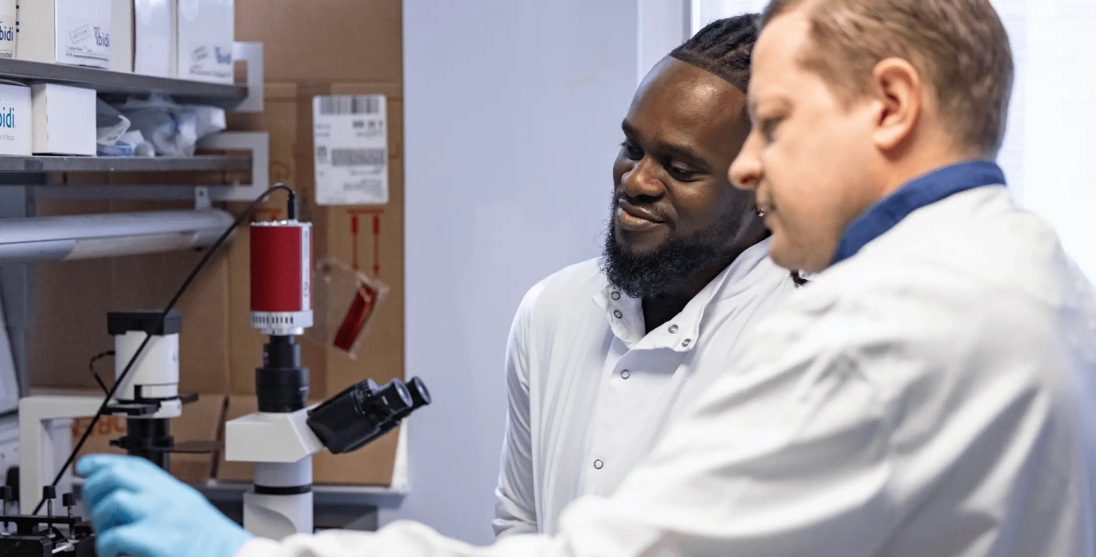 Two biopharmaceutical researchers collaborating in a laboratory setting, examining data under a microscope.